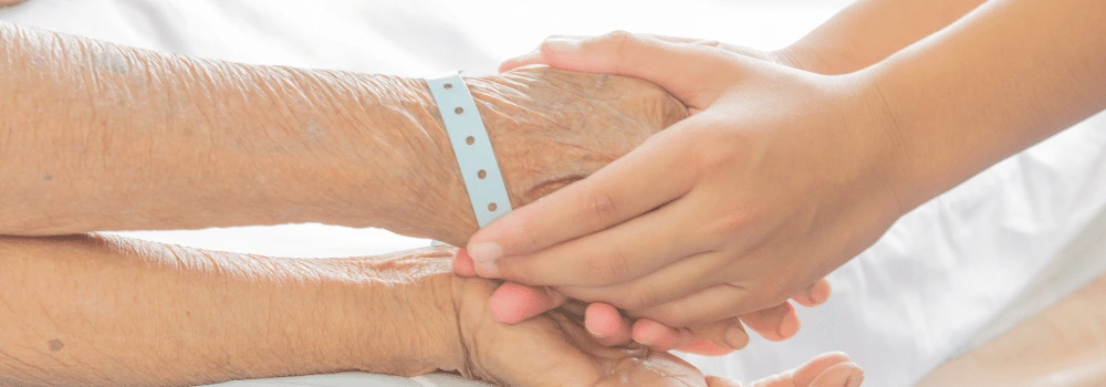Yngre person som håller en äldre persons händer i sina händer
