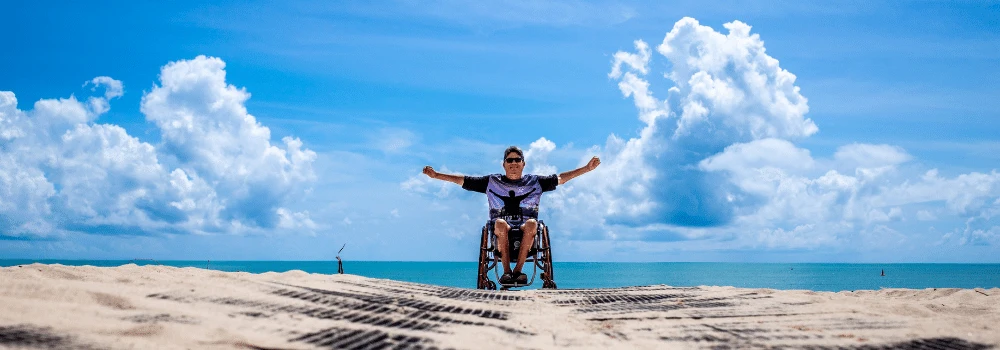 Man i rullstol med utsträckta armar med en klarblå bakgrund av himmel och hav